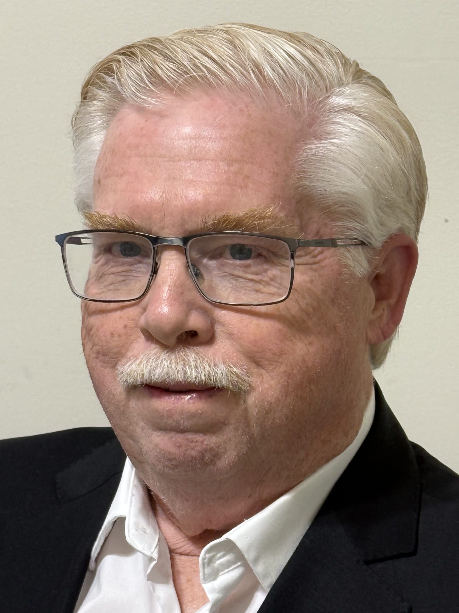 Blonde woman smiling, wearing a blue floral shirt, against a white backdrop.