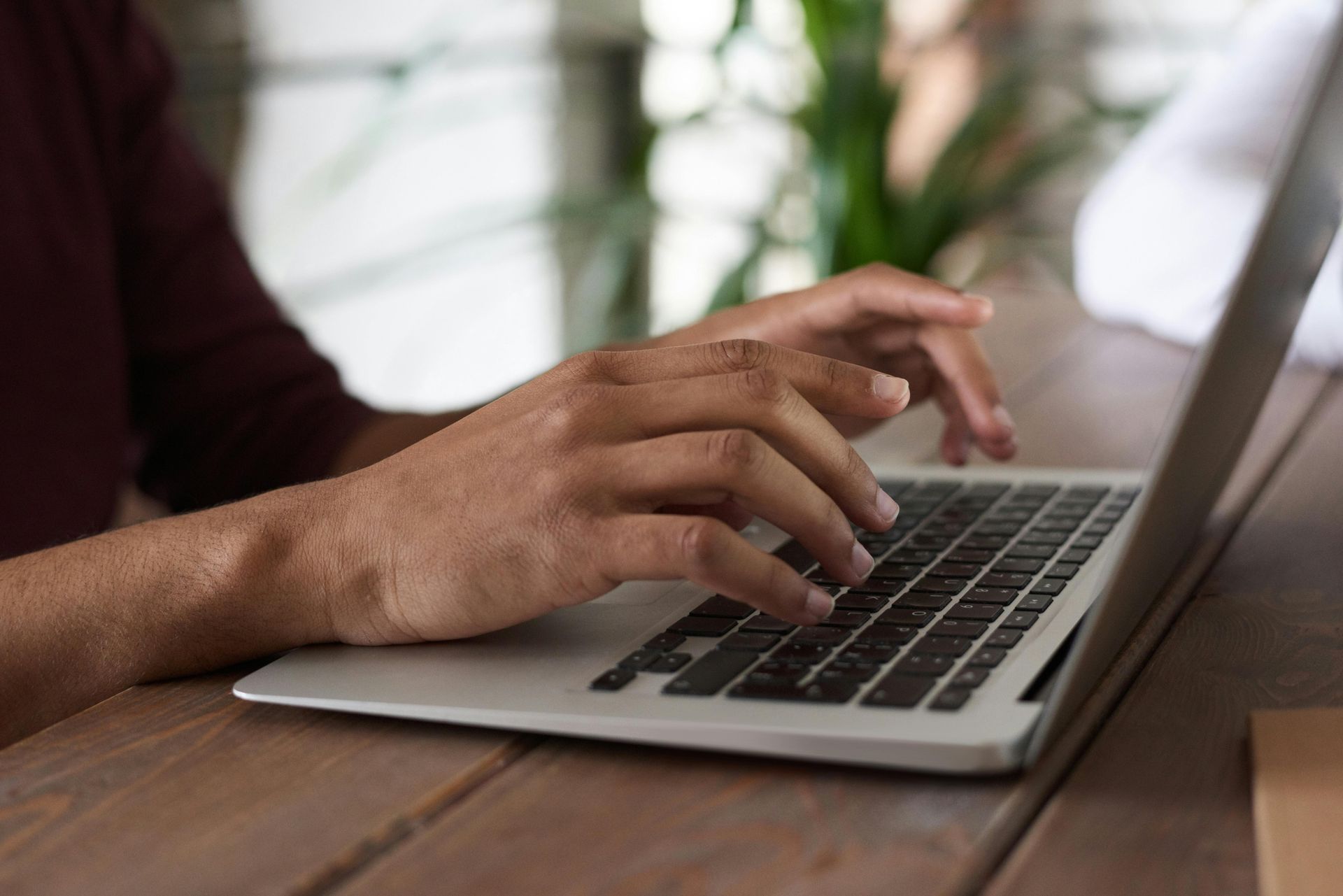 Person writing in a notebook at a table with a laptop and another person using a phone.