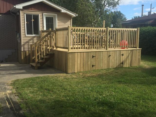 Une terrasse en bois avec des escaliers se trouve dans la cour d'une maison.