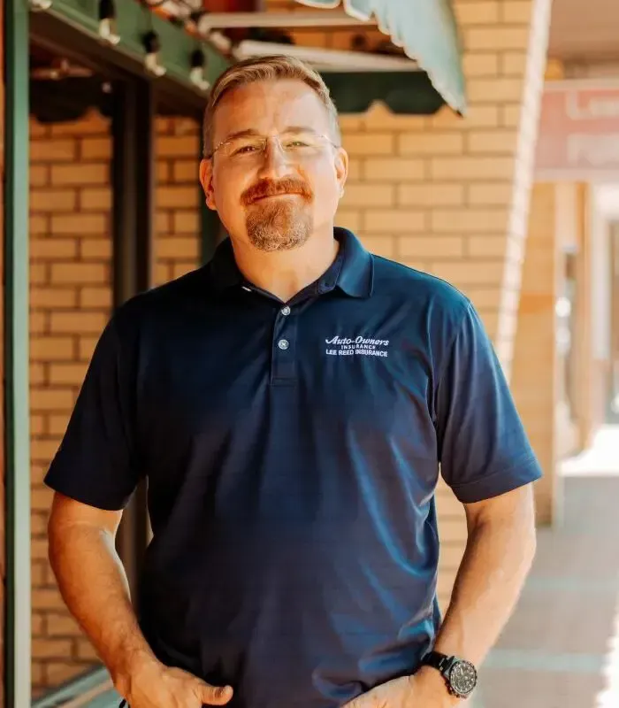 Man in blue polo shirt with glasses, standing in front of a brick building.