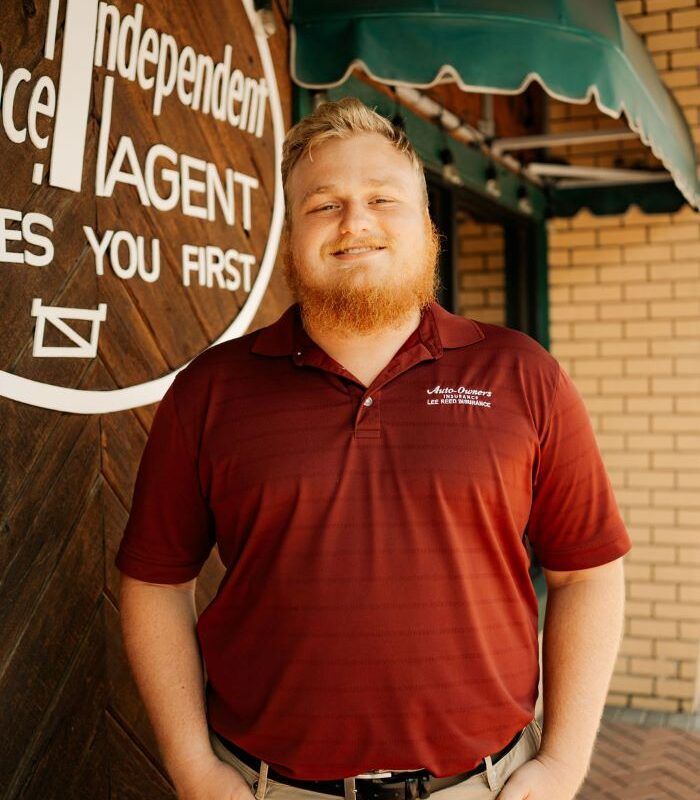 Blonde man with red beard in maroon polo shirt stands outside a building.