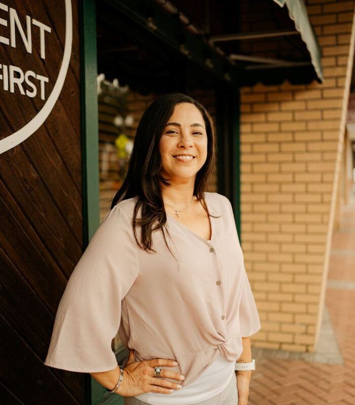 Woman in pink blouse smiling outside a brick building.