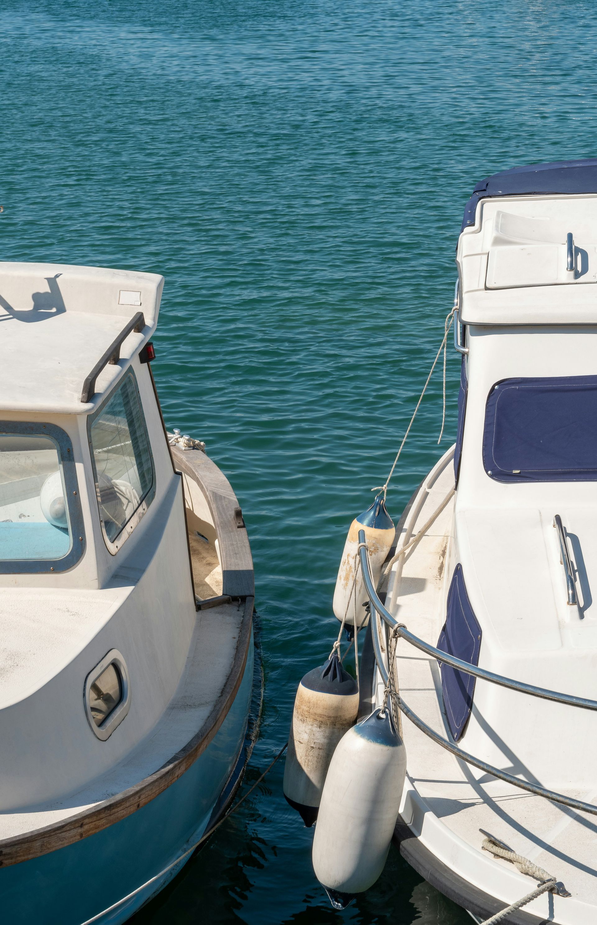 Two white and blue boats docked in the water, fenders separating them.
