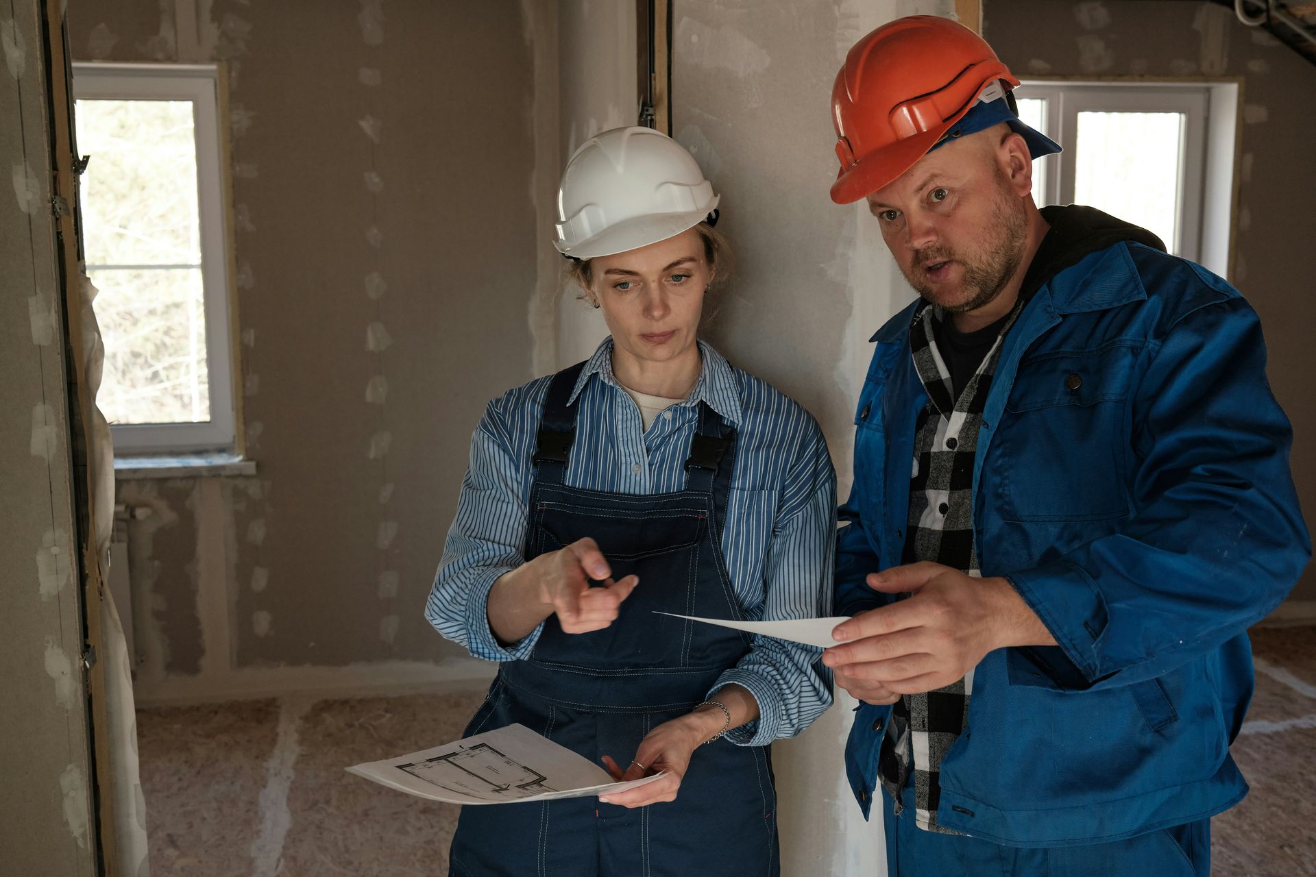 Construction workers, a man and a woman, reviewing blueprints at a construction site.