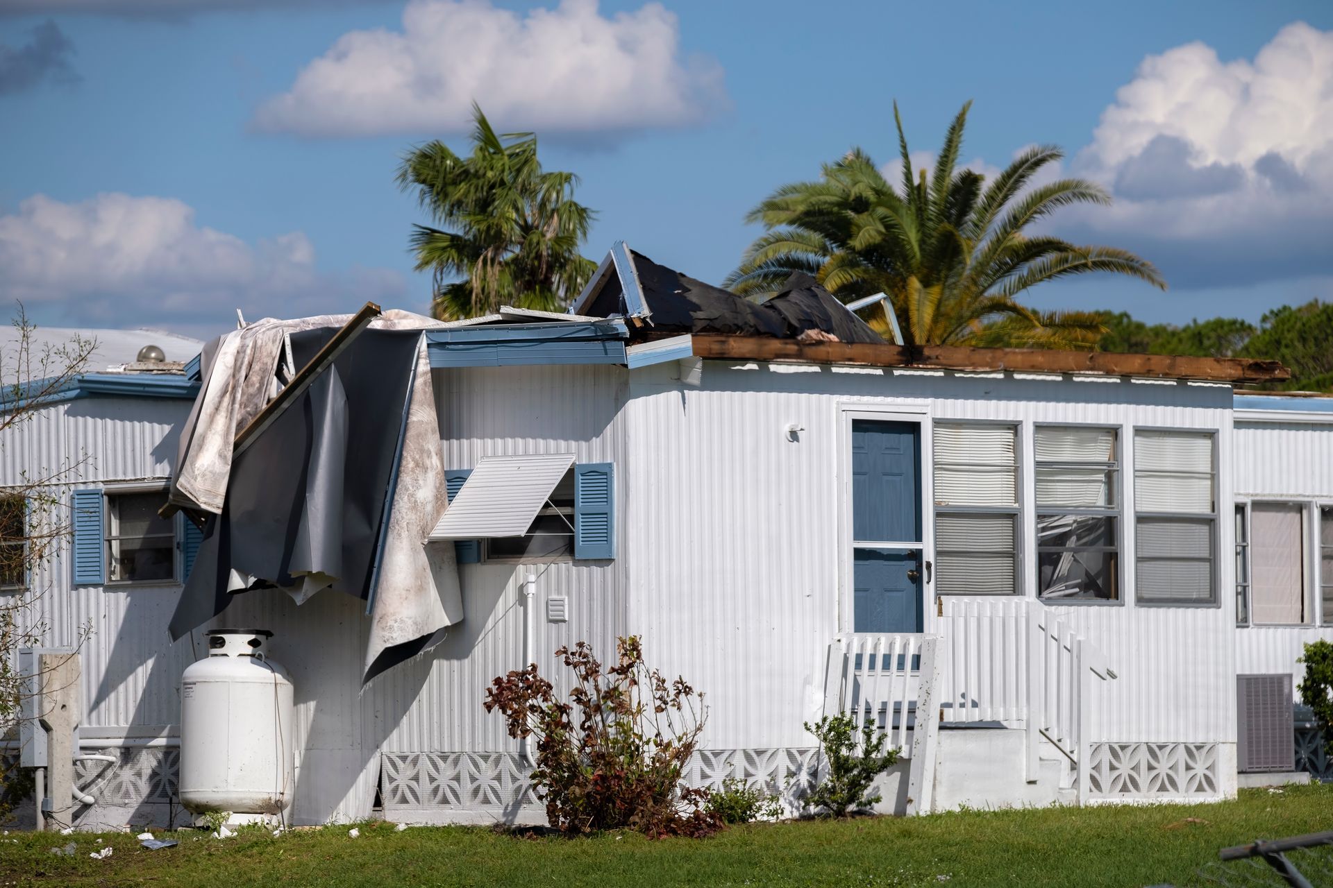 Mobile home with significant roof damage and debris, likely from a storm.