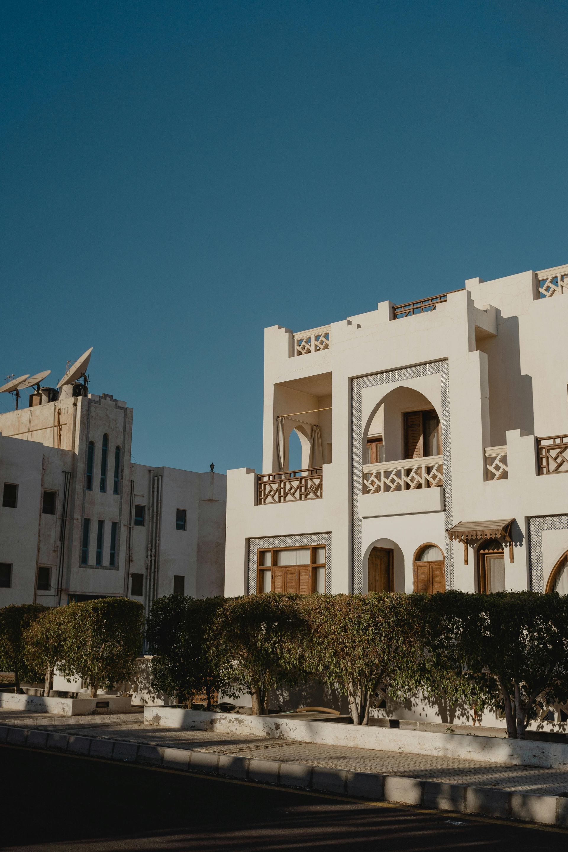 White stucco buildings with arched windows, greenery, and a blue sky.