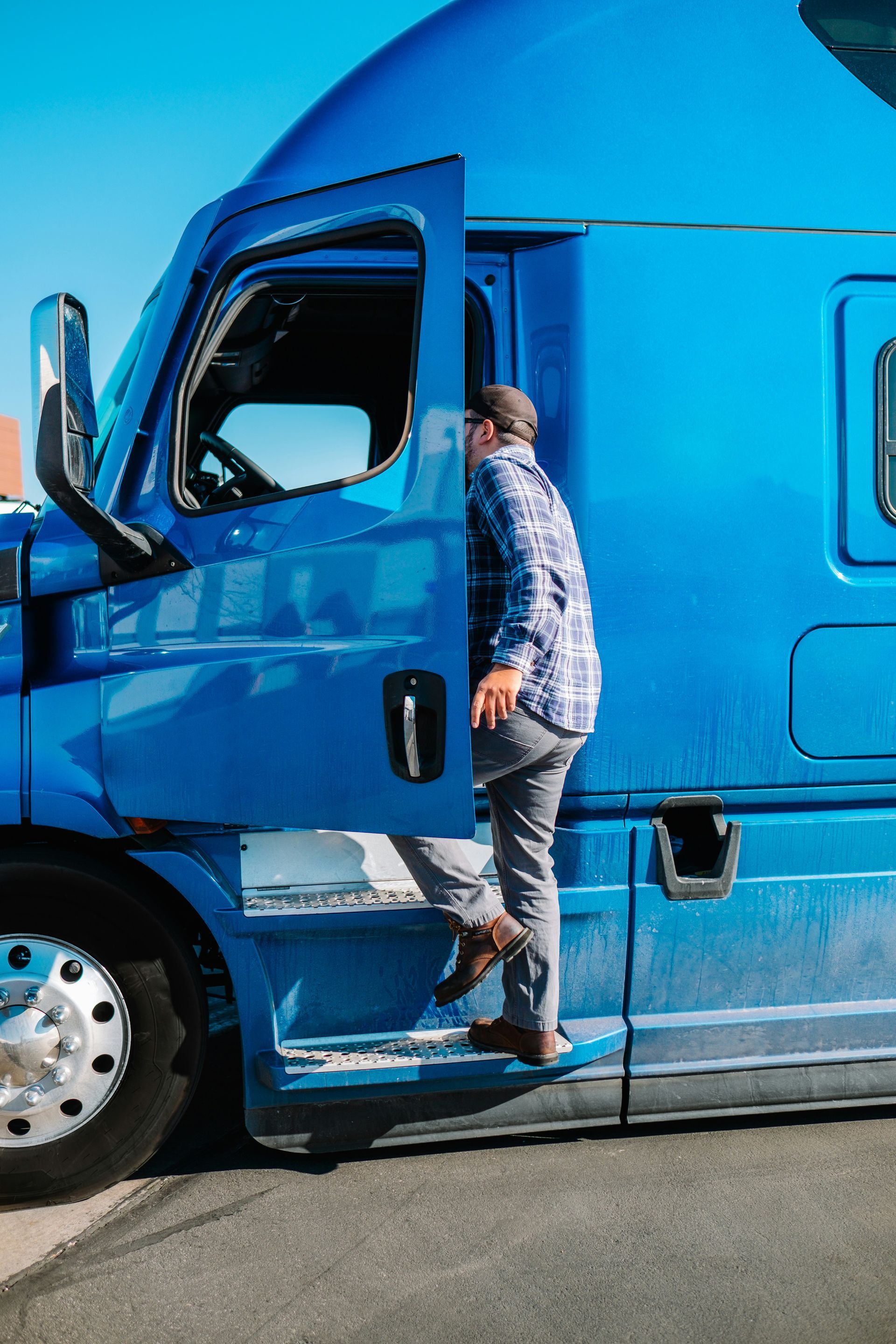 Man exiting a blue semi-truck, stepping down onto the side; sunny outdoors.