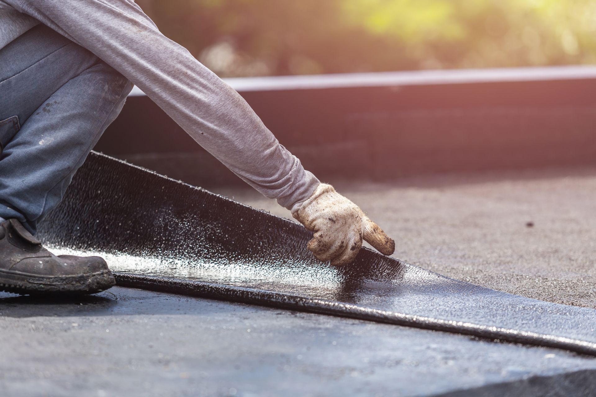 Close-up of a roofer, performing flat roof repair services by installing tar foil on a rooftop.
