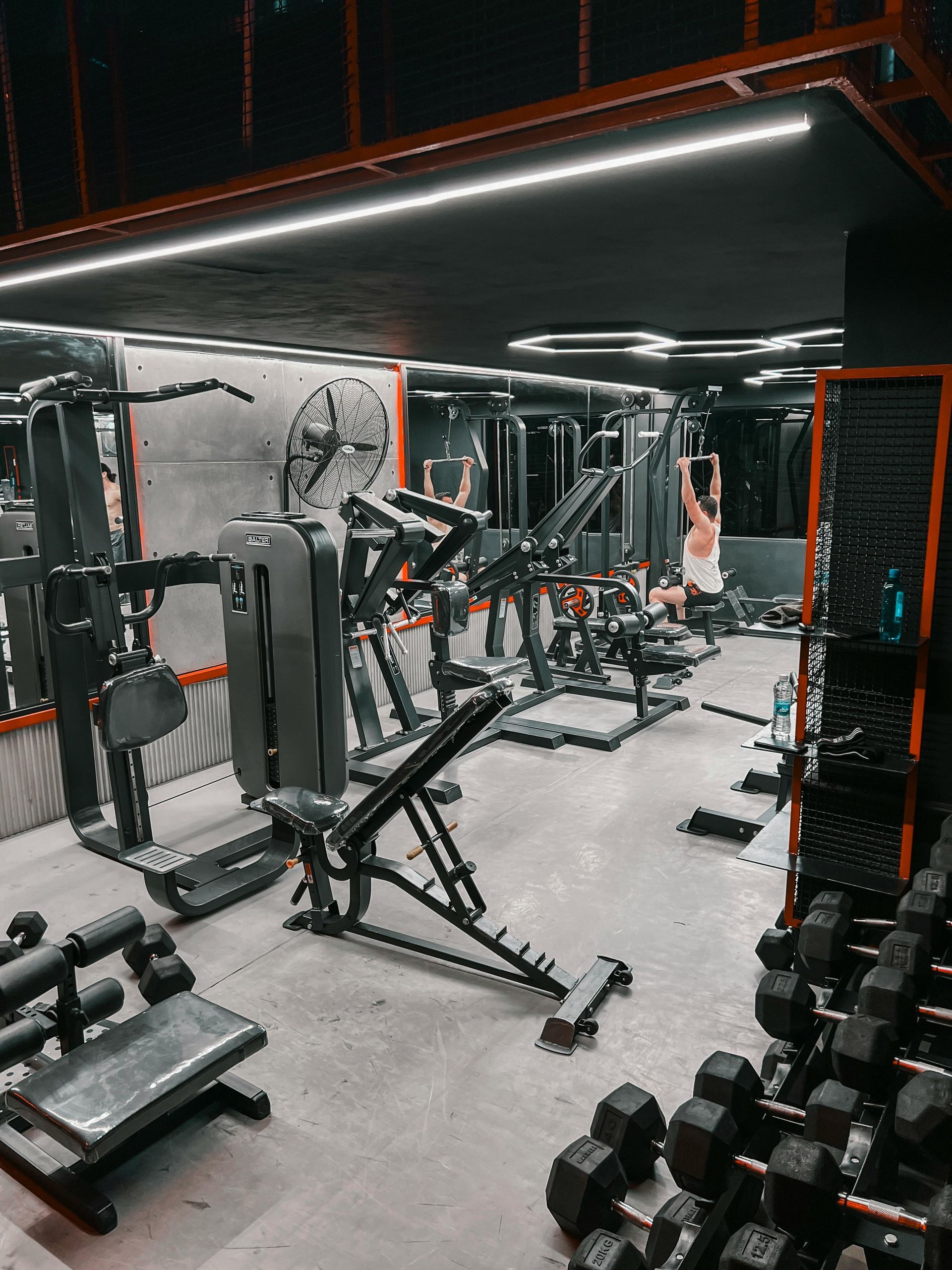 Modern gym interior with cable machines, mirrors, and dumbbells under orange accent lighting