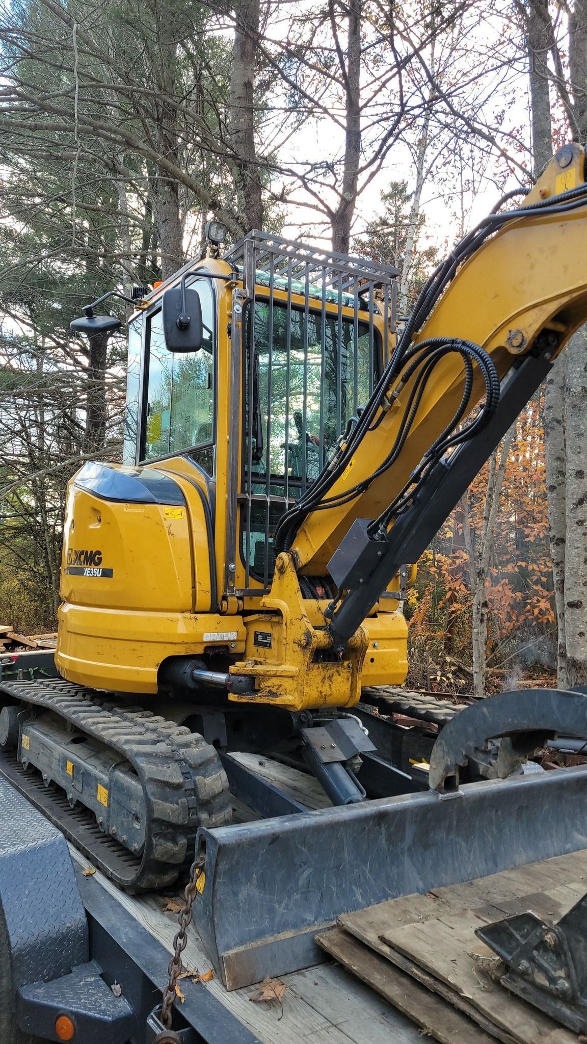 A yellow excavator is sitting on top of a trailer in the woods.