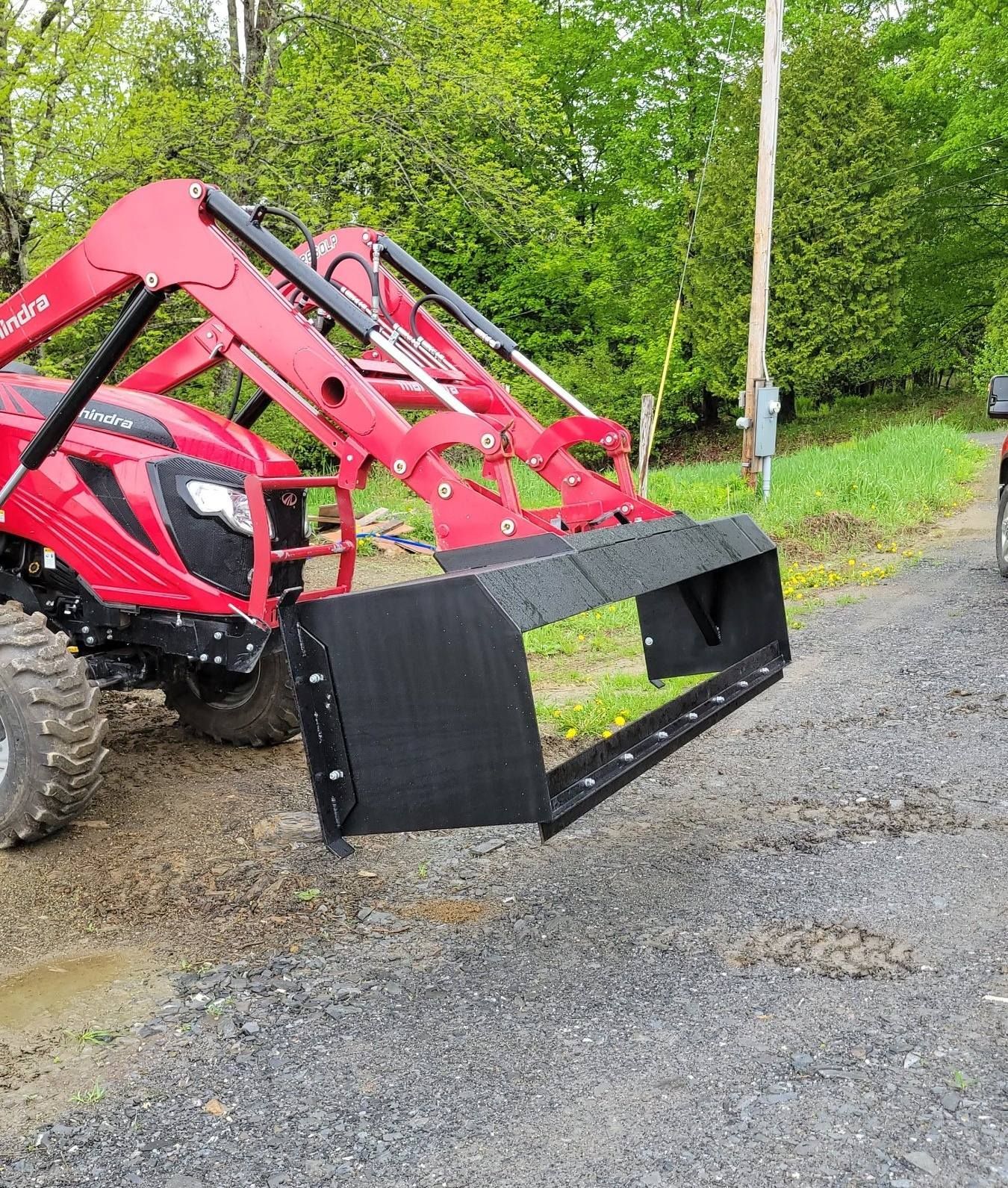A red tractor with a black bucket is parked on the side of the road.