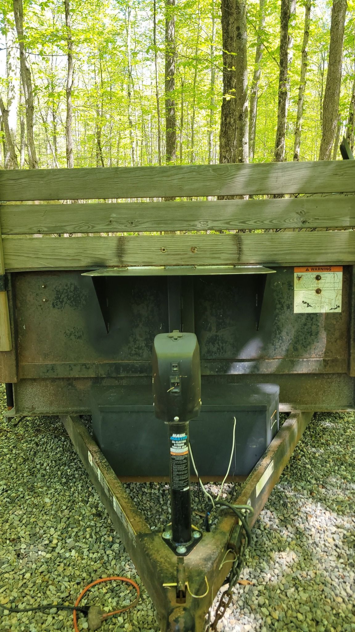 A trailer is parked on a gravel road in the woods.