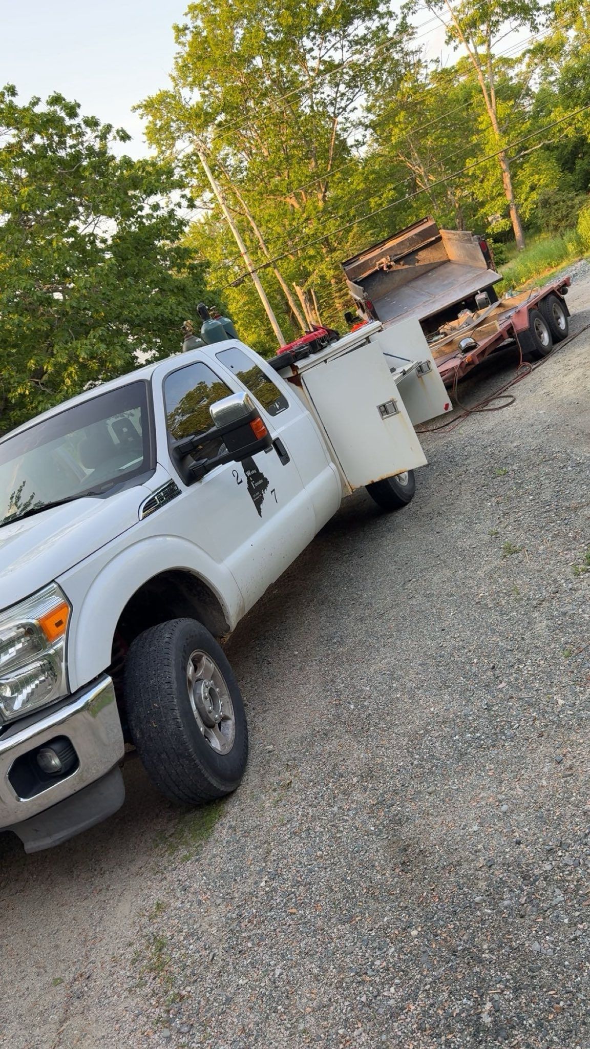 A white tow truck is parked on the side of the road next to a trailer.
