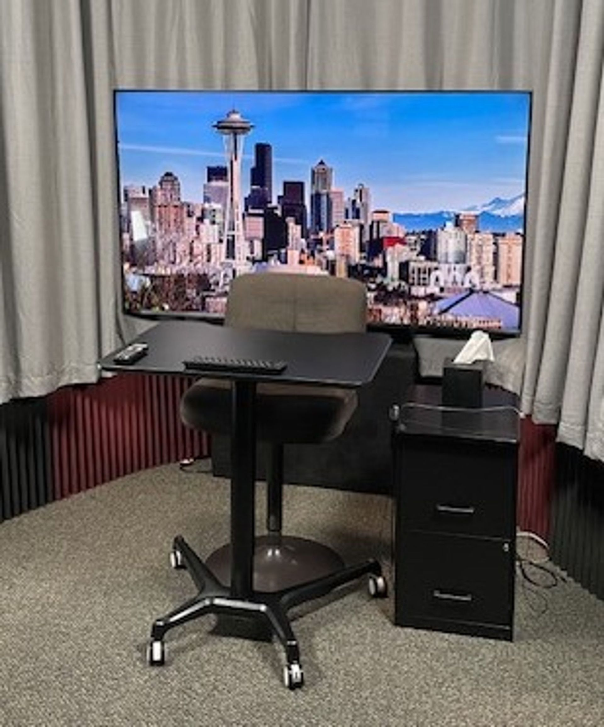 Small office desk with chair, filing cabinet, and a Seattle skyline screen behind curtains.