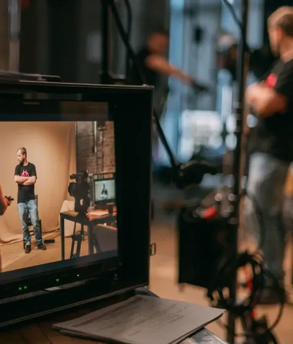 Camera monitor showing a person standing in a studio with filming equipment in the background