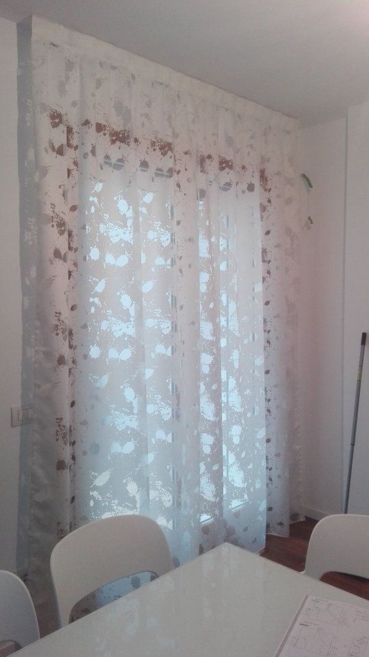 Una sala da pranzo con tavolo e sedie e una finestra con tende bianche.