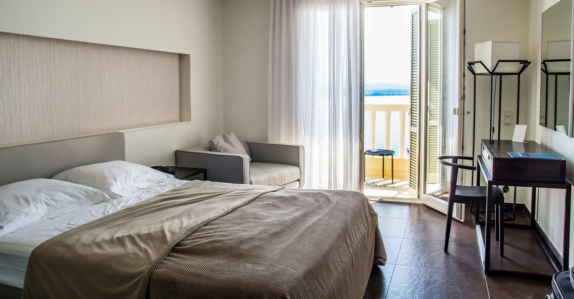 Una camera d'albergo con un letto, una scrivania, una sedia e un balcone.