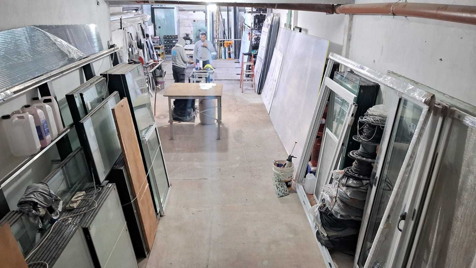 Interior de un taller; estanterías, mesas y diversos materiales de construcción; una persona es visible en el centro.