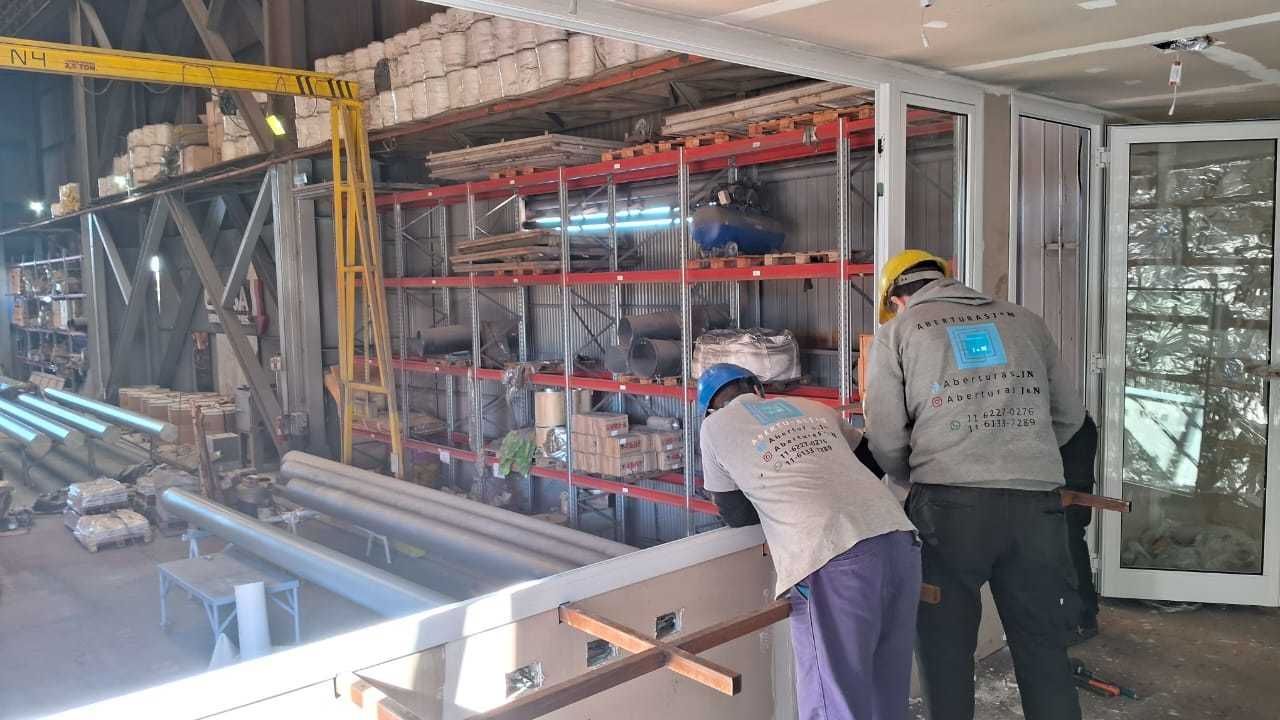 Dos trabajadores de la construcción instalando un marco de ventana dentro de un almacén con estanterías.