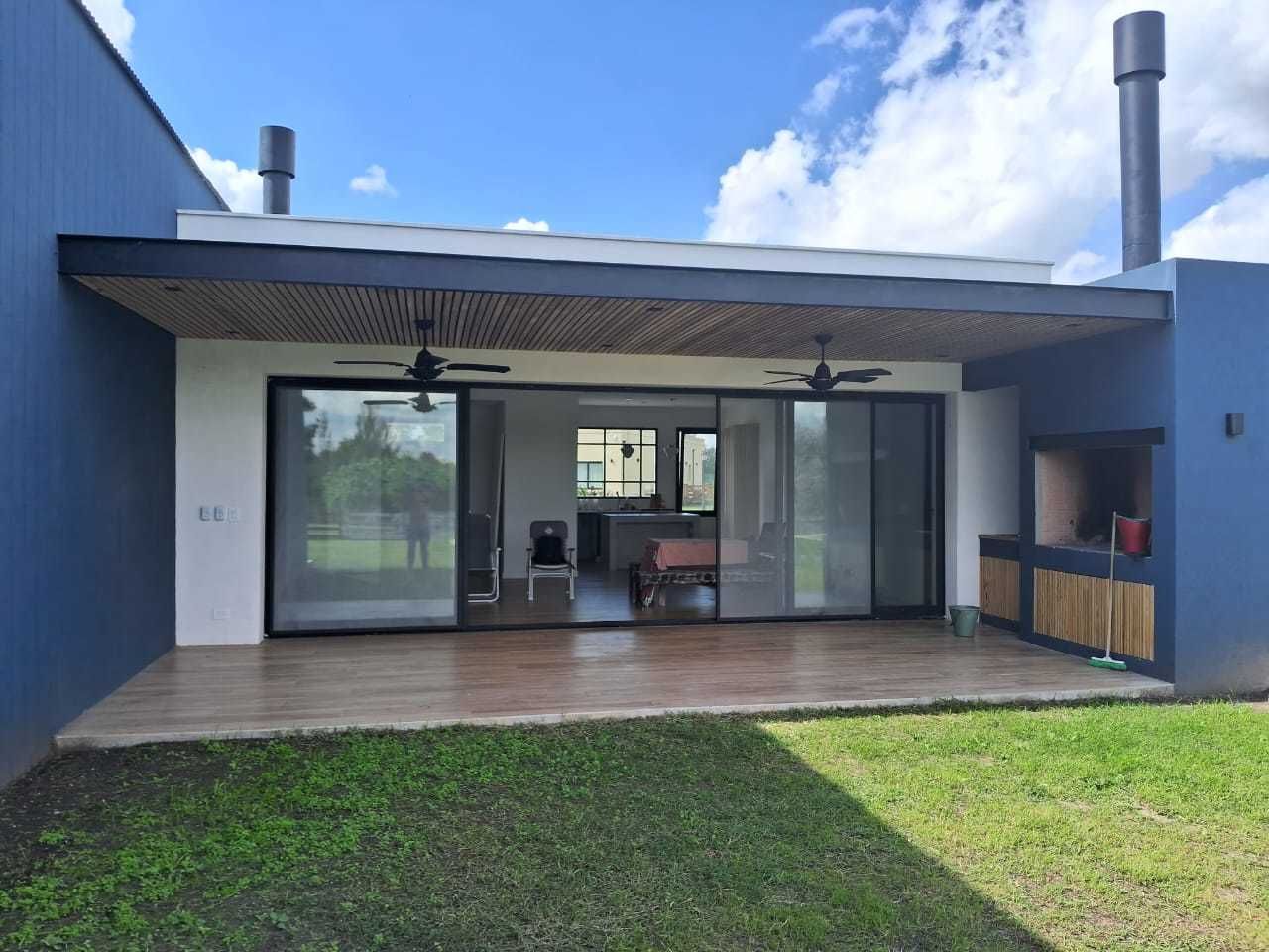 Vista exterior de una casa moderna con patio, parrilla y puertas corredizas de vidrio que conducen al interior.