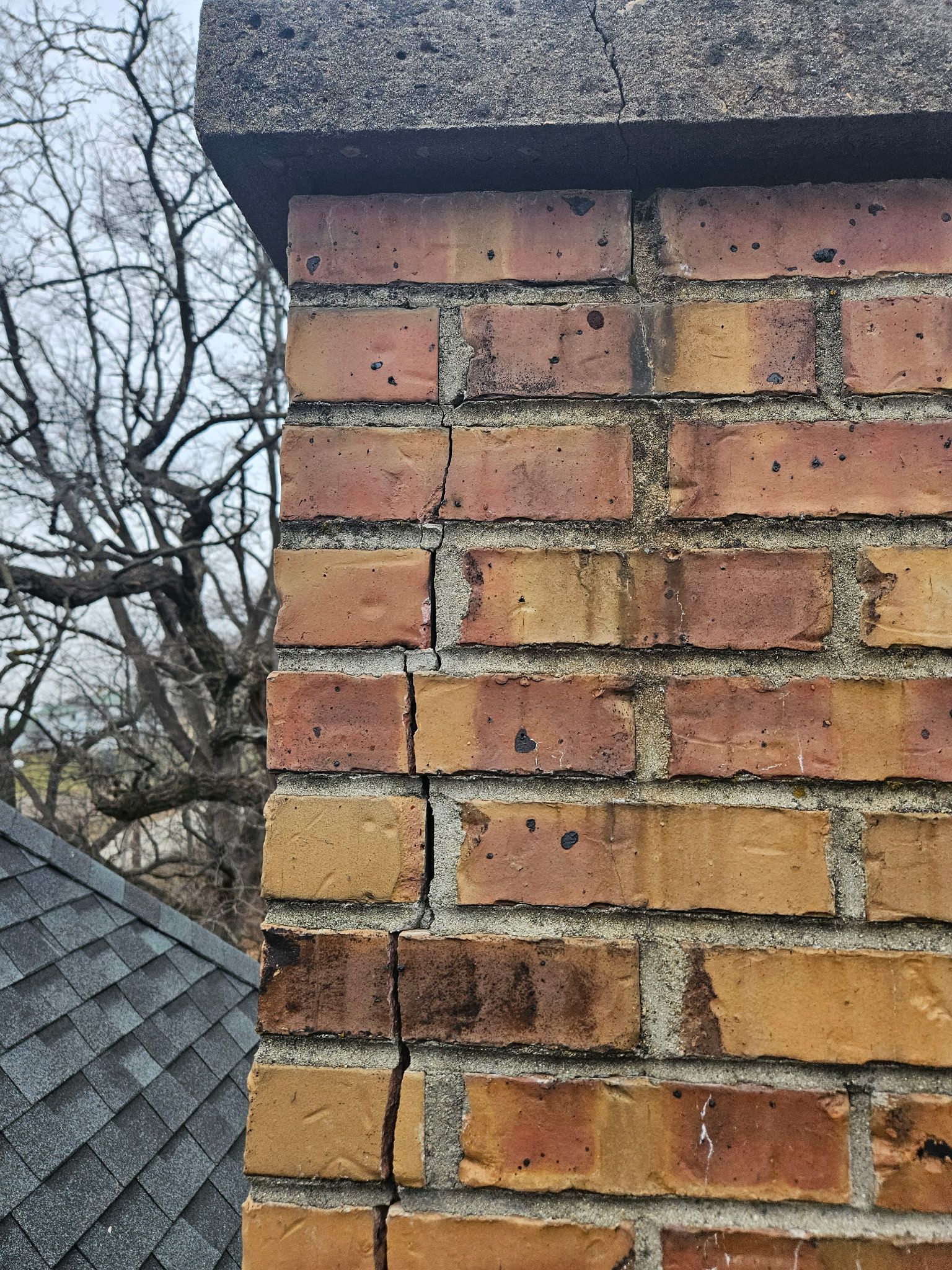 A close up of a brick chimney with a roof in the background.