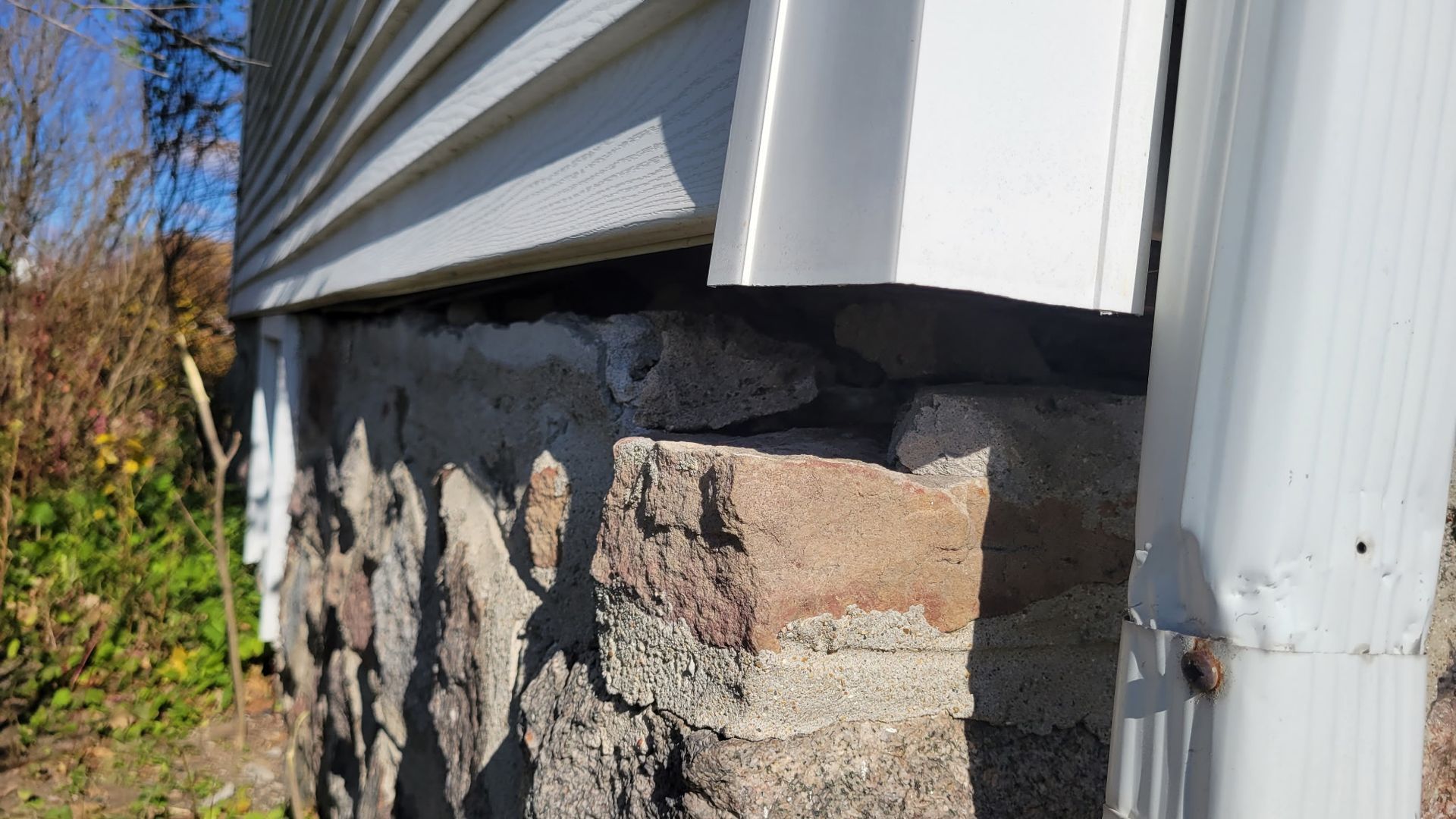 A close up of a brick wall next to a house with a white siding.