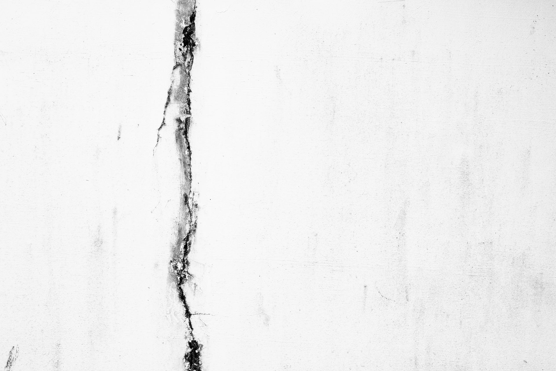 White wall with a vertical crack, darker areas around the fissure.