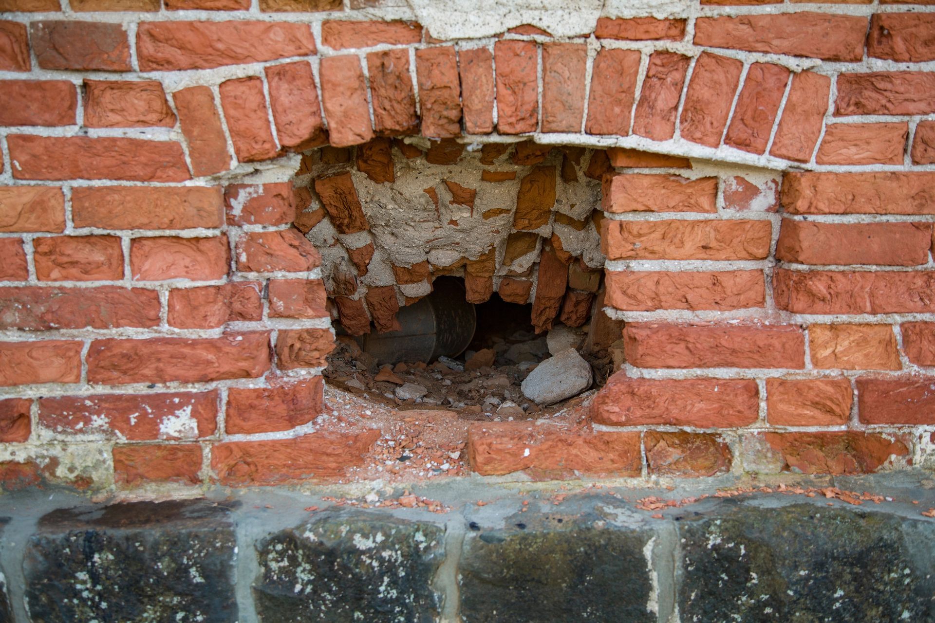 A hole in a brick wall with a rock in it.