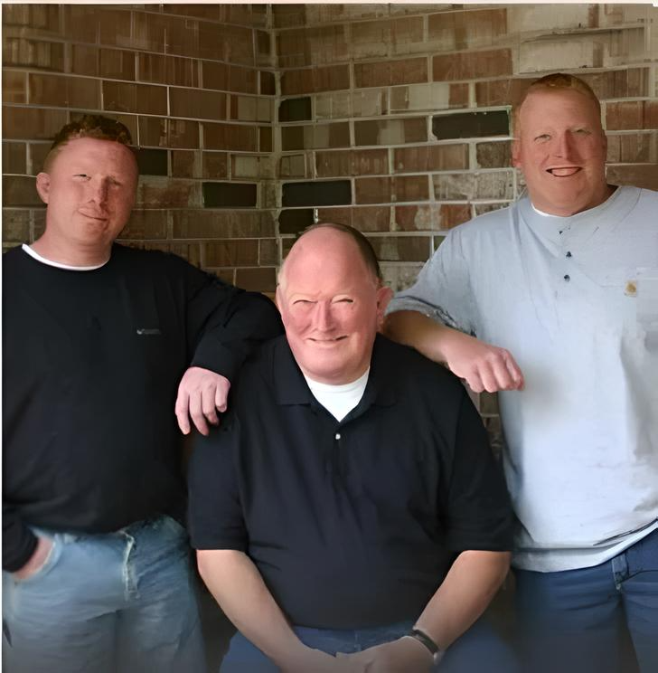 Three men posing for a picture in front of a brick wall
