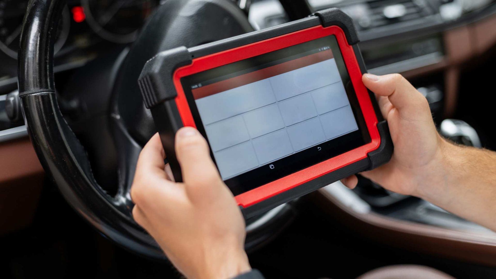 Hands holding a red tablet in a car, showing a diagnostic screen.