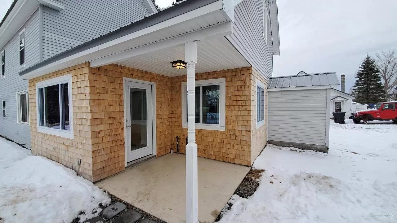 Small, partially built addition to a white house with a porch. Exterior features tan siding and windows, with snow on the ground.