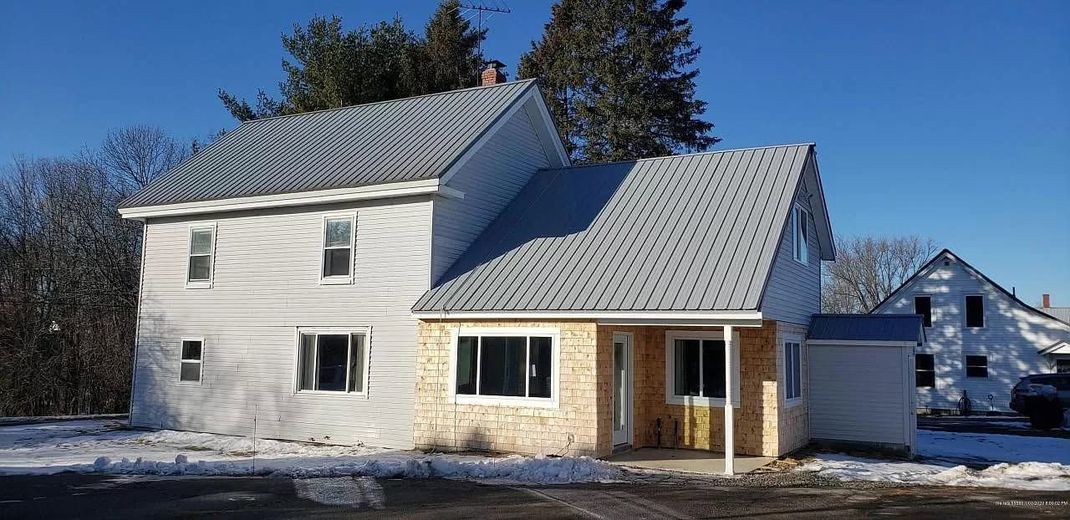 A two-story house with a new addition and light snow on the ground. The sky is clear blue.