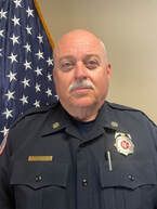 A man in a police uniform is standing in front of an american flag.