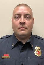 A man in a police uniform is standing in front of a white wall.