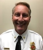 A man in a white shirt and black tie is smiling for the camera.