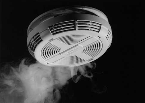 A black and white photo of a smoke detector with smoke coming out of it.