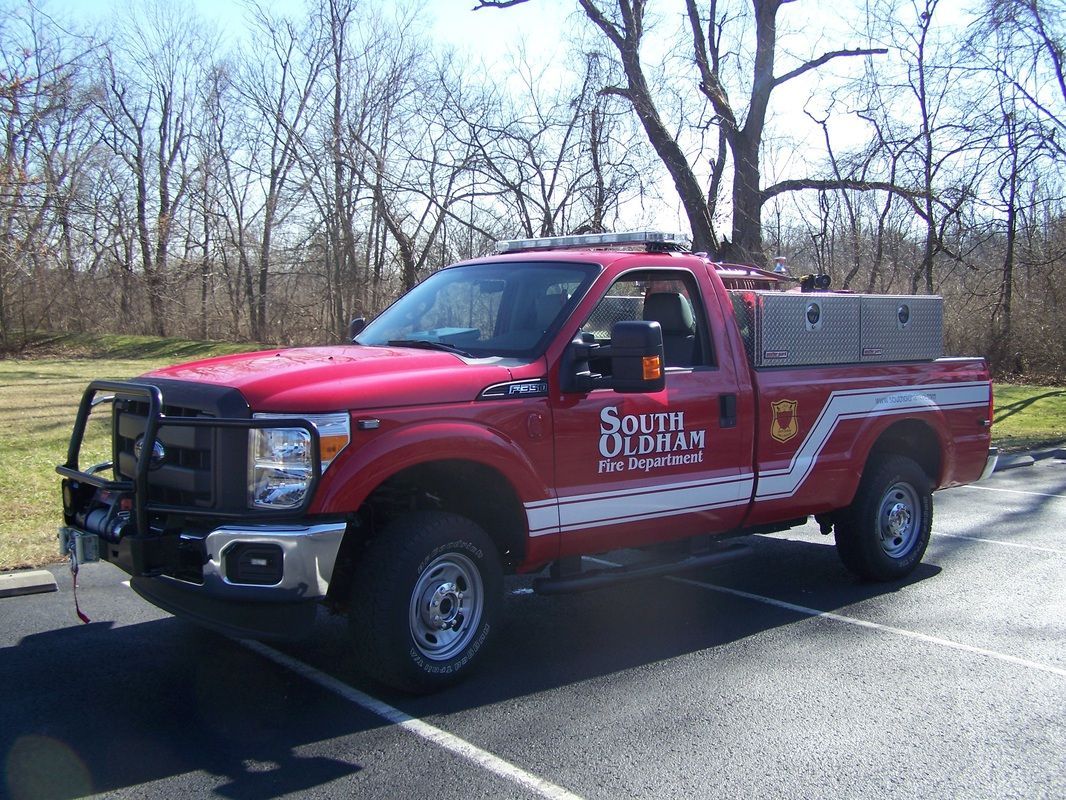 A red truck is parked in a parking lot with trees in the background.