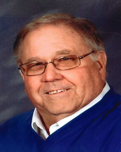 A man wearing glasses and a blue sweater smiles for the camera