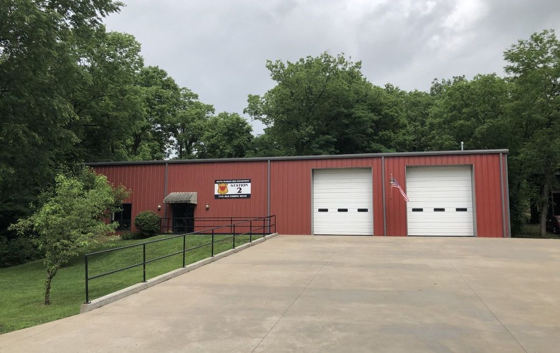 A red building with two white garage doors is surrounded by trees.