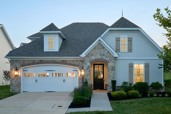 Cottage-style home with stone and white siding, a white garage door, and black front door, at dusk.