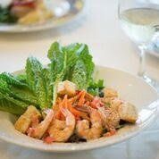 Plate of shrimp and salad with a glass of white wine in the background.