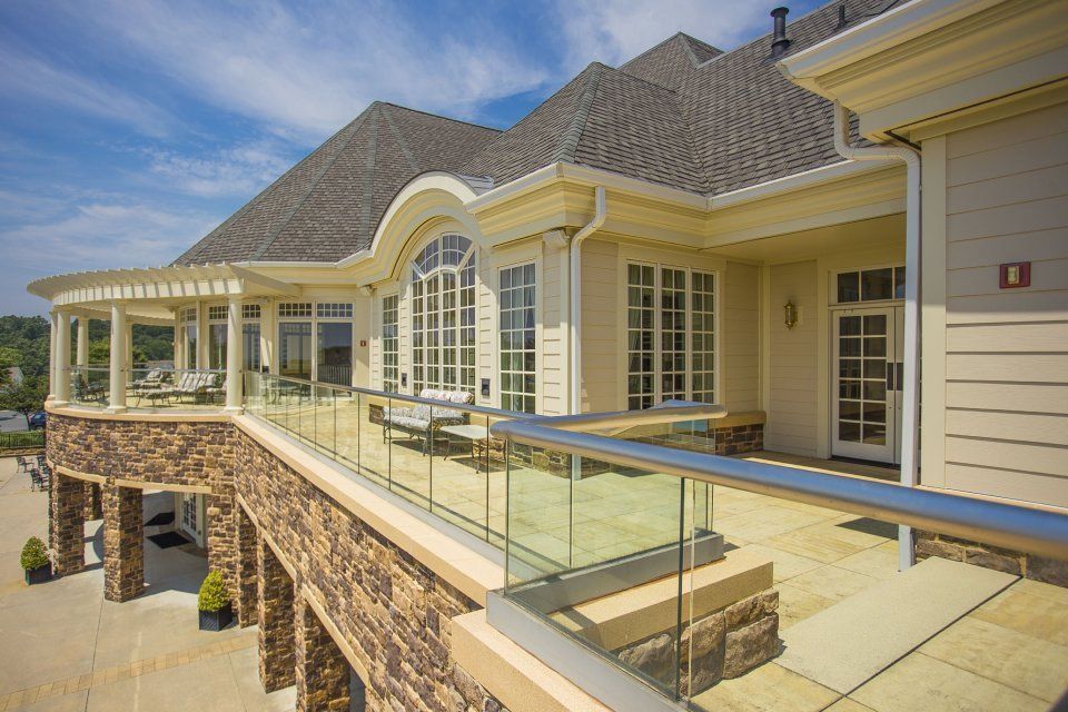 Exterior view of a building with a stone facade, a glass balcony, and a pergola, under a blue sky.