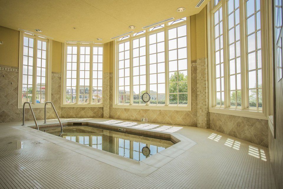 Indoor spa with a jacuzzi, surrounded by large windows, tiles, and light yellow walls.
