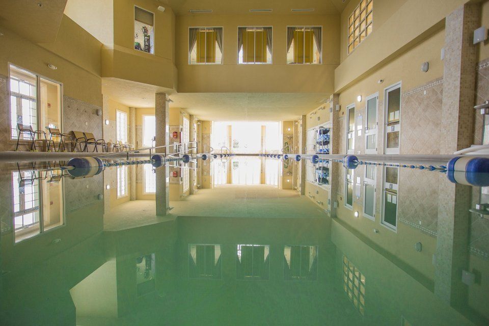 Indoor swimming pool with beige walls, windows, and reflected light.