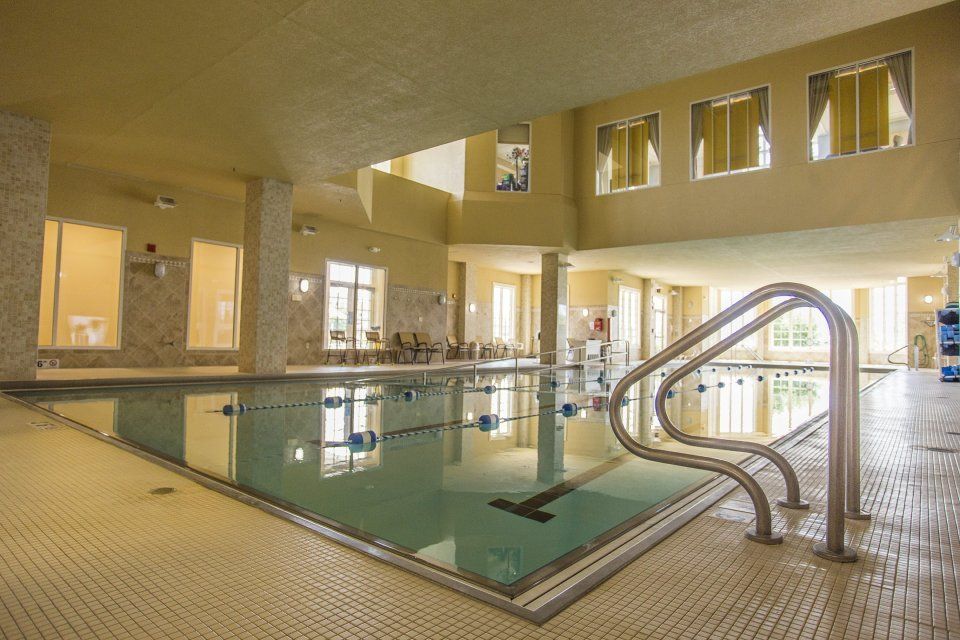 Indoor swimming pool with handrails, tiled floor, and windows.