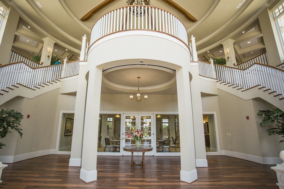 Grand foyer with a dual staircase and a second-floor balcony. White and beige color scheme. Wooden floors.