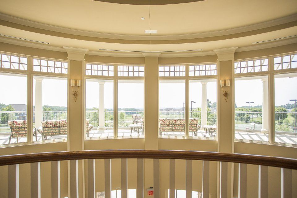 Interior view of a rotunda with large windows overlooking a patio with seating. Beige walls and a wooden railing.