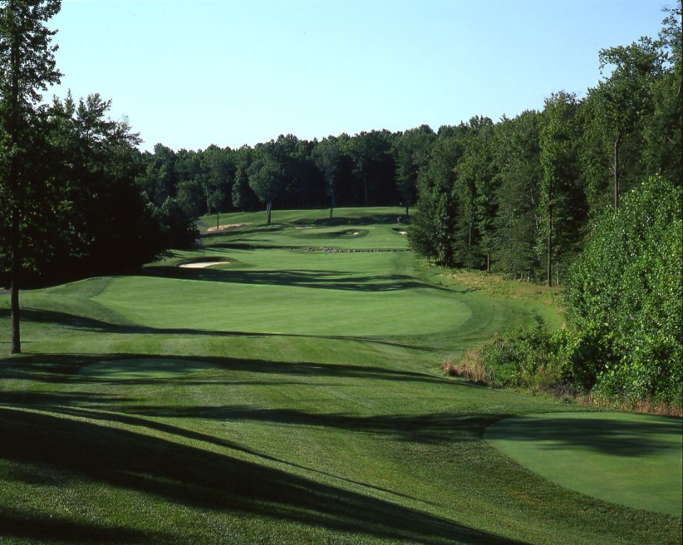 Golf course fairway lined by trees on a sunny day.