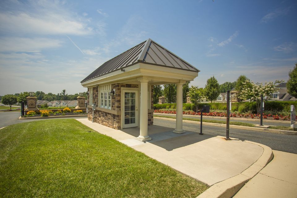 Security booth at gated community entrance with stone exterior and green lawn.