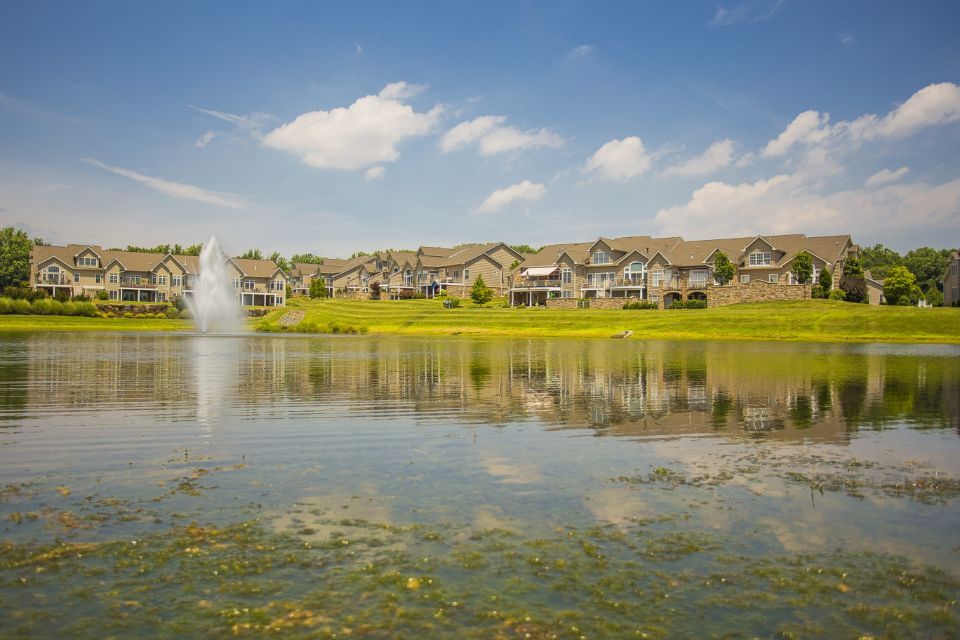 Houses line a lake with a fountain. Blue sky with clouds.